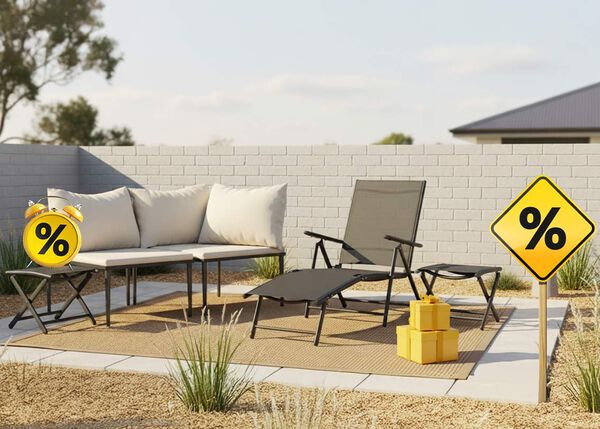 A grey outdoor lounge set with cream cushions, a matching sunlounger and side tables, yellow gift boxes, a sign, and a clock with discount icons, all on a styled patio.