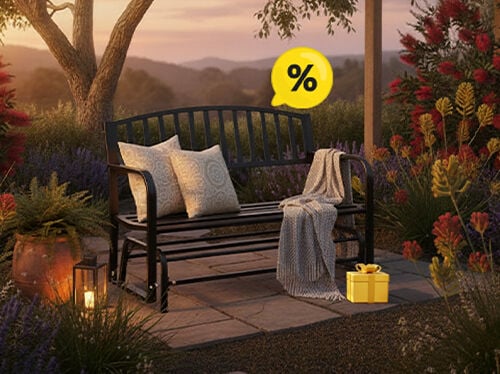 A black metal garden bench with patterned cushions and a throw blanket, next to a yellow gift box and a discount icon, in a sunset garden setting. Click to see the products in the offer.