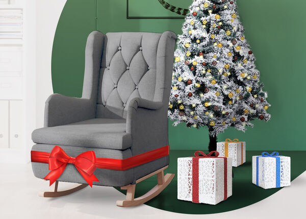 Grey upholstered rocking chair wrapped in a red bow, next to a Christmas tree and gift boxes, in a styled living room.