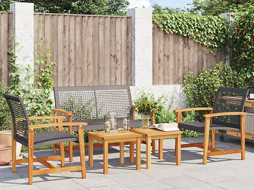 Rattan furniture set with table arranged in a backyard, placed in front of a wooden wall with green plants in the background. Click to see the products in the offer. 