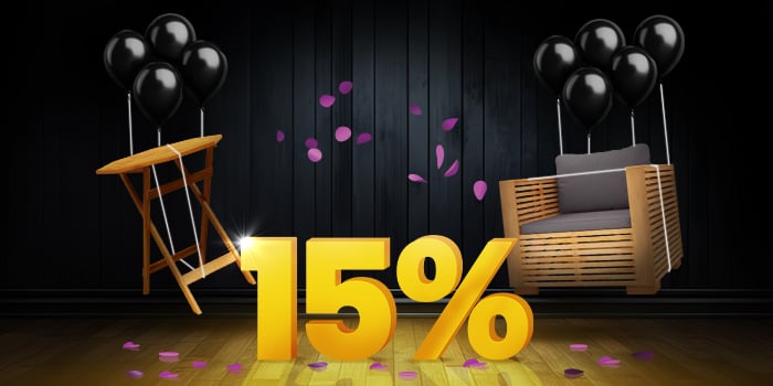 Wooden folding side table and wooden outdoor armchair with dark cushions lifted by black balloons and surrounded by purple confetti, with a large yellow 15% sign on a dark background. Click to shop the collection.