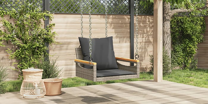 Rattan outdoor swing bench with dark cushions on a patio.